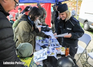 Policjantka uśmiecha się do dziecka na stoisku promocyjnym Policji.