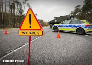Znak drogowy z napisem &quot;wypadek&quot;, a za nim policyjny radiowóz.