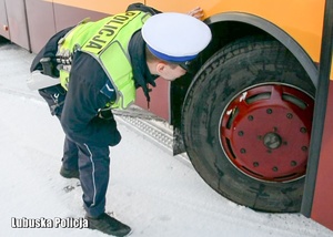 Policjant drogówki sprawdza stan opony w autobusie.