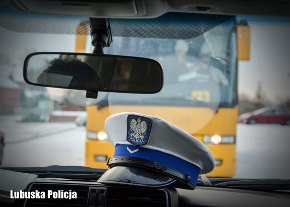 Policyjna czapka w radiowozie policyjnym, przed którym stoi autobus.