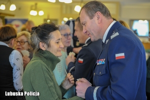 Komendant Wojewódzki Policji podczas składania życzeń i łamania się opłatkiem ze starszą kobietą.
