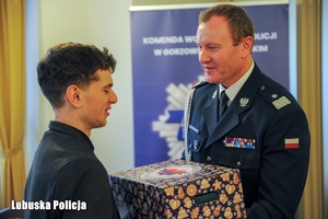 Komendant Wojewódzki Policji wręcza prezent młodemu mężczyźnie.