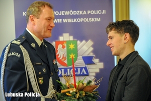 Komendant Wojewódzki Policji przyjmuje prezent świąteczny od młodego mężczyzny.