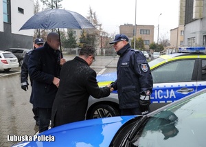 Policjant odbiera gratulacje od mężczyzny podczas uroczystości przekazania nowego radiowozu.