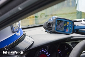Czapka policjanta ruchhu drogowego oraz urządzenie do pomiaru prędkości na desce rozdzielczej pojazdu