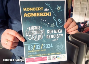 Plakat dotyczący koncertu charytatywnego w dłoniach policjanta.
