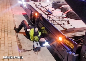 Policjant podczas przeprowadzania czynności diagnostycznych pod pojazdem ciężarowym.