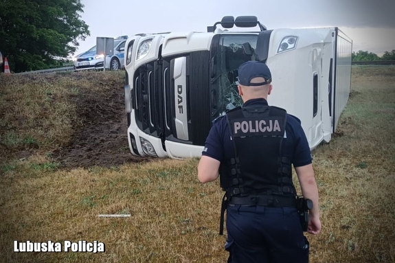 policjant stoi przy przewróconej ciężarówce