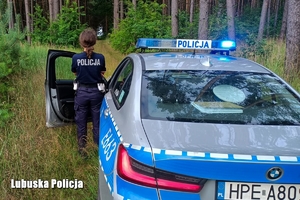 Policjantka oraz pojazd służbowy, w tle widoczna droga leśna