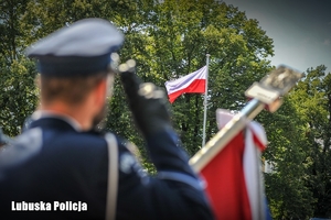 Funkcjonariusz policji składa honor przed masztem flagowym