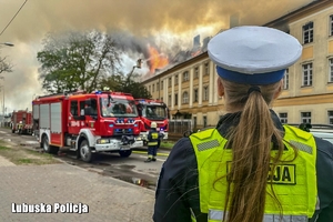 Policjantka zabezpieczająca miejsce zdarzenia podczas akcji gaśniczej strażaków