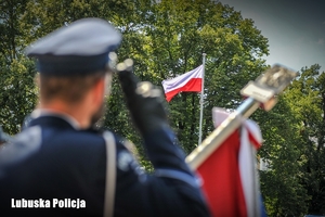 Policjant oddaje honor, w tle widoczna flaga Polski