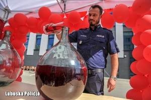 policjant wlewa czerwony płyn do butli