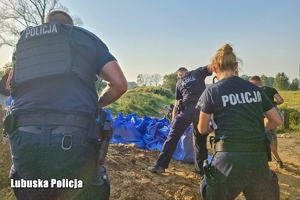 policjanci pomagają ładować worki z piaskiem