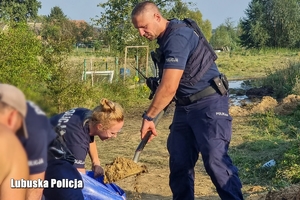 policjanci pomagają ładować worki z piaskiem