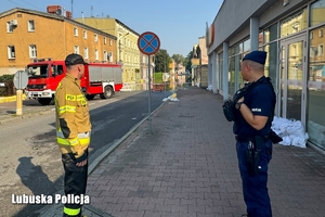 Policjant wraz z strażakiem patrzy w stronę zalanej drogi