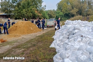 policjanci pomagają szykować worki z piaskiem