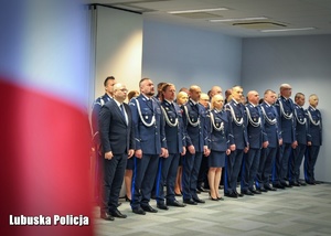 Flaga Polski, a w tle policjanci stojący w rzędzie.