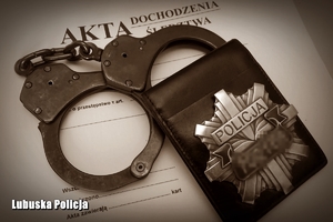 Kajdanki i odznaka policyjna na aktach postępowania.