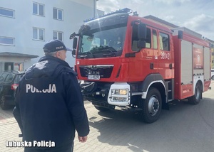 Policjant na tle wozu strażackiego.