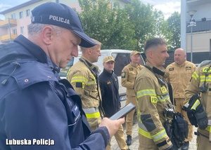 Policjant stojący obok strażaków.