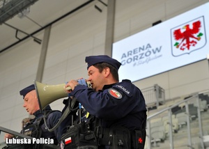 Policjant przez megafon wydaje polecenia.