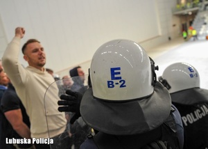 Policjant oddziałów prewencji, a w tle kibic.