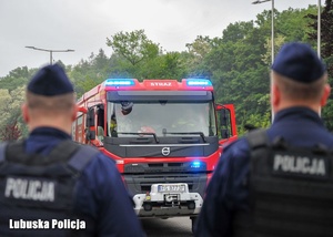 Policjanci na tle samochodu straży pożarnej.