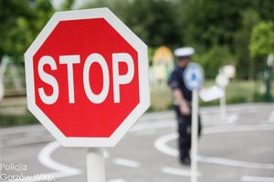 Znak STOP, a w tle policjant przeprowadzający egzamin na kartę rowerową.