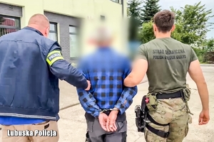 Policjant i strażnik graniczny prowadzą zatrzymanego mężczyznę.