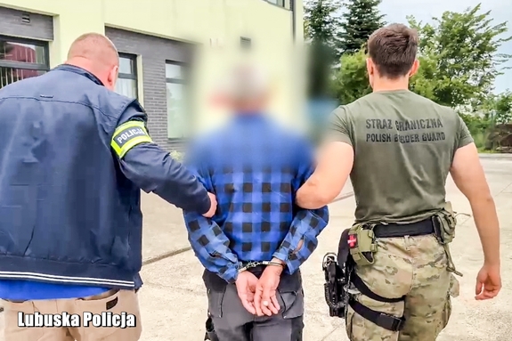 Policjant i strażnik graniczny prowadzą zatrzymanego mężczyznę.
