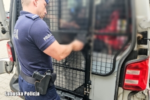 Policjant zamyka drzwi od policyjnego busa.