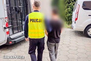 Policjant prowadzi zatrzymaną osobę.