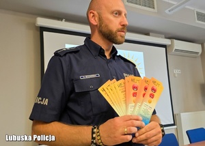 Policjant trzyma w dłoni ulotki profilaktyczne.