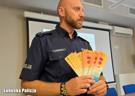 Policjant trzyma w dłoni ulotki profilaktyczne.