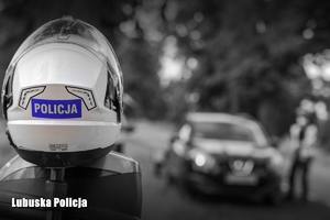 Policyjny kask motocyklowy, a w tle kontrola drogowa przeprowadzana przez policjantów.
