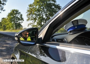 Widok policjanta odbijający się w lusterku bocznym radiowozu.
