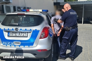 policjant prowadzi zatrzymanego mężczyznę do radiowozu