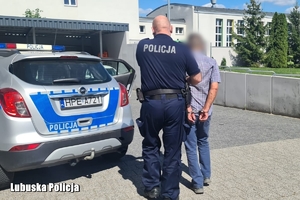policjant prowadzi zatrzymanego mężczyznę do radiowozu