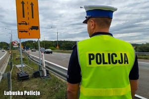 Policjant idący poboczem drogi.