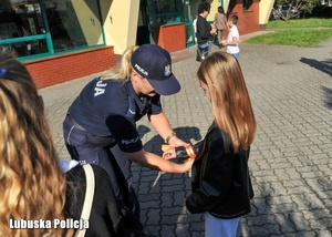 Policjantka przypina dziecku element odblaskowy.
