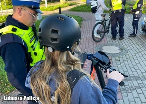 Policjant podczas kontroli drogowej osoby na hulajnodze elektrycznej.