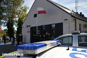 Policyjny radiowóz, a w tle policjanci przy posterunku.