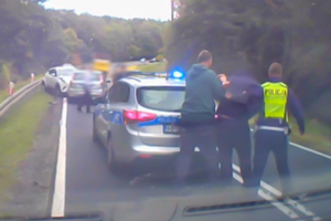 policjant prowadzi zatrzymanego mężczyznę do radiowozu