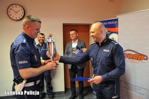 Policjant wręcza puchar dla drugiego funkcjonariusza