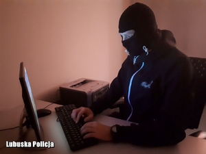 Mężczyzna w kominiarce siedzący przed komputerem.