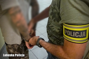 policjant trzyma osobę z kajdankami na rękach