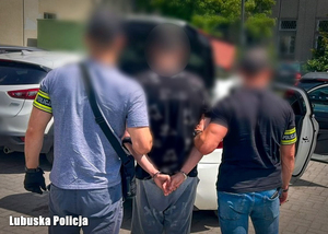 Nieumundurowani policjanci podczas przeprowadzenia zatrzymanego mężczyzny w kajdankach.
