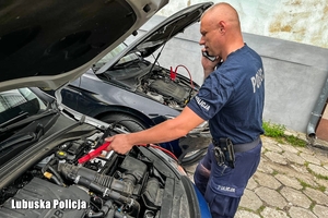 Policjant podłącza klemy do radiowozu.