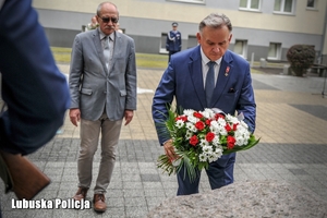 Mężczyźni składają kwiaty przy pomniku poświęconym poległym policjantom.